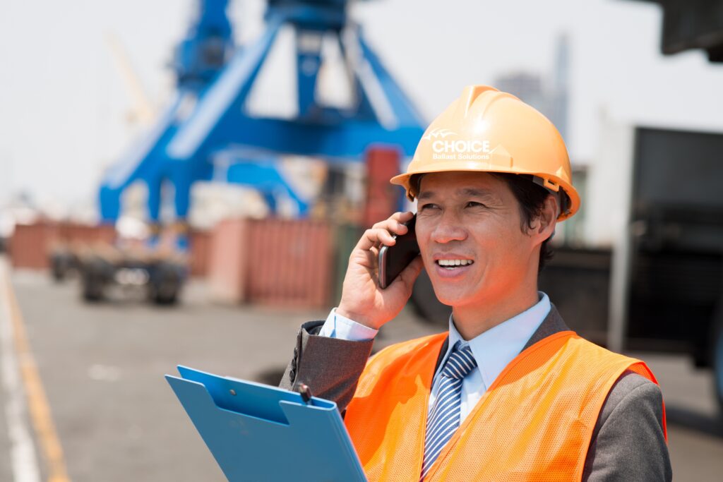 Person on the phone in shipyard with a Choice Ballast hardhat and clipboard